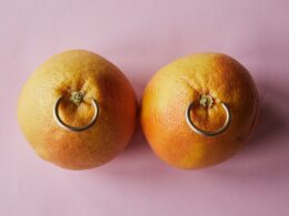 Fresh mandarins with earrings placed on pink surface