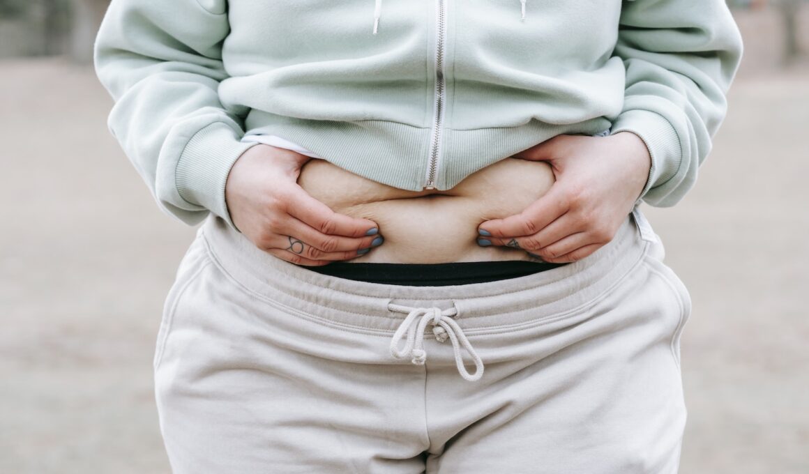 Crop anonymous plus sized female in casual hoodie touching and showing fat on belly while standing in park