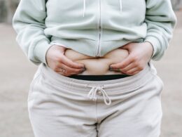 Crop anonymous plus sized female in casual hoodie touching and showing fat on belly while standing in park