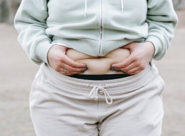 Crop anonymous plus sized female in casual hoodie touching and showing fat on belly while standing in park