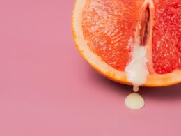 High angle of closeup of half of fresh orange grapefruit as symbol of vagina with sperm placed on pink surface in studio