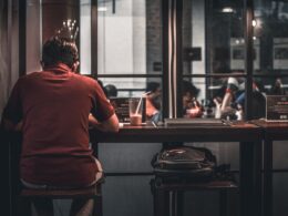 man sitting on brown wooden bar stool beside backpack on wooden bar stool