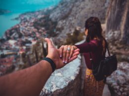 woman holding man's hand while looking on scenery of building beside body of water during daytime