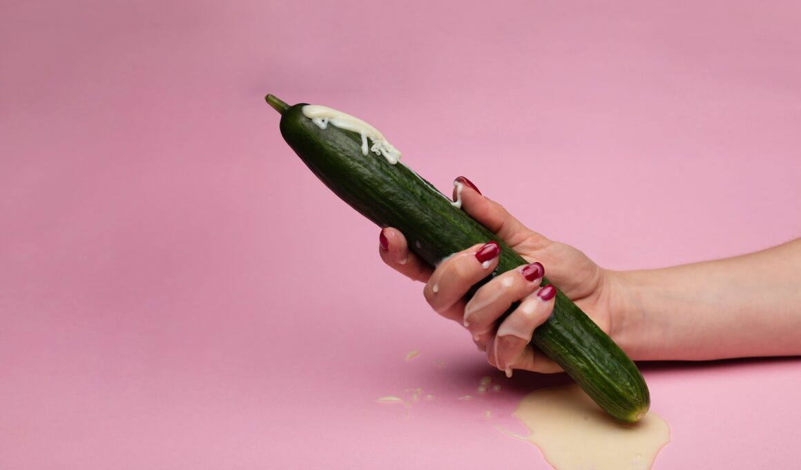 person holding green cucumber on pink surface