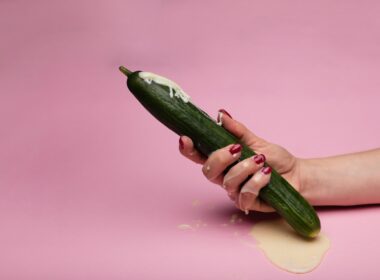 person holding green cucumber on pink surface